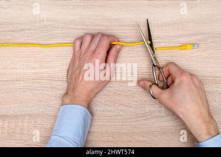 Internet-Zensor schneidet ein gelbes Netzwerkkabel über Holzhintergrund.eingeschränkter Internetzugang Konzept Stockfoto