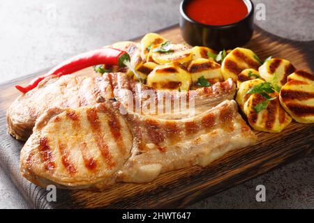 Scharf gegrillte saftige Schweinekoteletts mit Streifen. Kartoffel, Chili auf altem Holzbrett auf dem Tisch Nahaufnahme. Horizontal Stockfoto