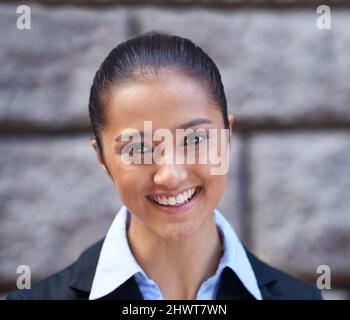 Sie meint Geschäfte. Ein Porträt einer schönen jungen Geschäftsfrau, die in der Stadt gegen eine Mauer steht. Stockfoto
