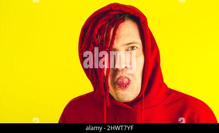 Junger Mann mit roten Dreadlocks, der die Kamera anschaut und seine Zunge zeigt. Gutaussehender Mann lächelt, streckt die Zunge aus und versteckt sie, flirtet Stockfoto