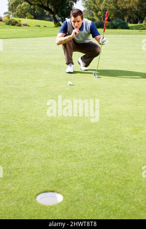Mann, der seine Optionen zum Putten einschätzt. Die ganze Länge des Mannes hocken auf dem Putting Green und Bewertung seiner Optionen, um den Ball zu werfen. Stockfoto