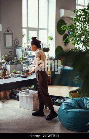 Konzentrierter Blumenhändler, der einem Polyeder-Florarium eine Bodenschicht hinzufügt Stockfoto