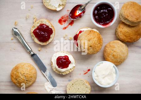 Blick von oben auf traditionelle britische Scones mit gerinnter Creme und Erdbeermarmelade für die Teestunde auf einem Holztisch Stockfoto