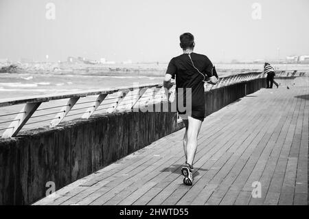 TEL AVIV-YAFO, ISRAEL - 24. FEBRUAR 2014: Mann mittleren Alters beim Joggen im alten Hafen von Tel Aviv. Der Hafen ist ein beliebtes Freizeit- und Geschäftsviertel. Schwarz-weiß Stockfoto