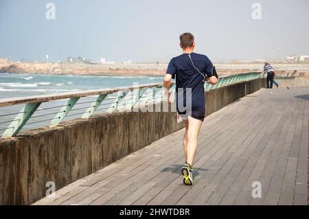 TEL AVIV-YAFO, ISRAEL - 24. FEBRUAR 2014: Mann mittleren Alters beim Joggen im alten Hafen von Tel Aviv. Der Hafen ist ein beliebtes Freizeit- und Geschäftsviertel Stockfoto