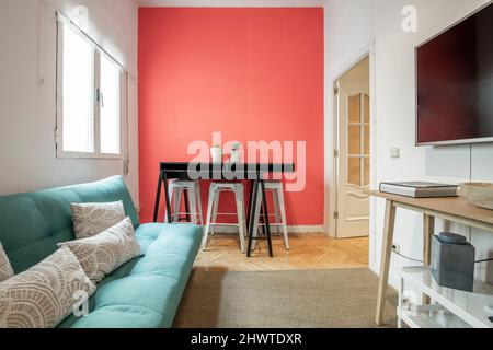 Wohnzimmer einer kurzfristigen Mietwohnung mit einem grünen Schlafsofa, einer rot gestrichenen Wand und einem Anrichte aus Eichenholz mit einem großen Fernseher darüber und Stockfoto