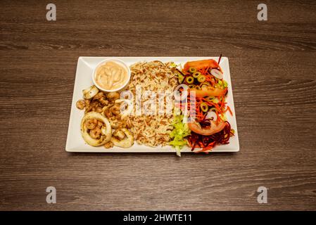 Eine Kombination aus Basmati-Reis mit Tomatensalat und geriebenem Gemüse, Sauce und sautierten Garnelen mit gebratenen Tintenfischringen Stockfoto