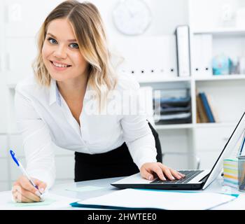 Aufmerksame Mädchen schreibt etwas auf ein Blatt Papier in modernen Büro Stockfoto