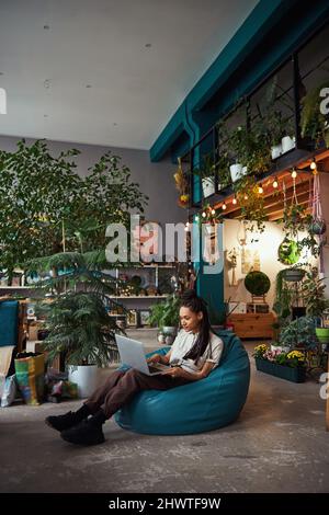 Ruhige, konzentrierte Frau, die in einer Werkstatt an ihrem Laptop arbeitet Stockfoto