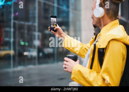 Fröhlicher Kerl mit Getränk, der Selfie im Freien nimmt Stockfoto