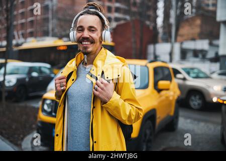 Fröhlicher bärtiger Mann, der im Freien Musik in Kopfhörern genießt Stockfoto