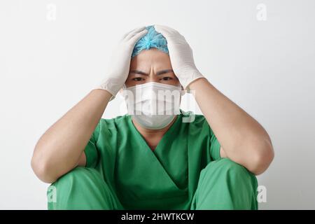 Gestresster müder Gesundheitsmitarbeiter, der nach einer langen Schicht gegen das Coronavirus auf dem Boden sitzt Stockfoto