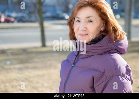 Eine attraktive ältere Frau schaut in die Kamera und lächelt. Straßenportrait. Stockfoto