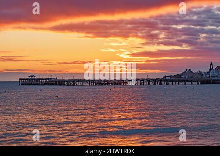 Ein wunderschöner orangefarbener Sonnenaufgang platzt über dem alten Swanage Pier, der sich vom Meer abspiegelt Stockfoto