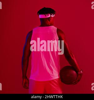 Wenn ich etwas liebe, gebe ich alles. Rot gefilterte Aufnahme eines jungen Sportlers, der mit einem Basketball im Studio posiert. Stockfoto