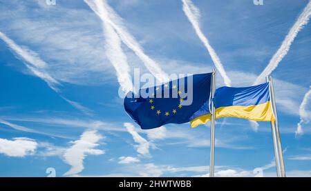 Flaggen der Ukraine und der EU, der Europäischen Union gegen blauen Himmel mit Luftfahrtinkongelstreifen. Konzeptbild: Keine Flugzone, Russland Ukraine-Konflikt, Krieg, Europa... Stockfoto