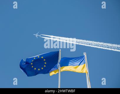 Flaggen der Ukraine und der EU, der Europäischen Union gegen blauen Himmel mit Luftfahrtinkongelstreifen. Konzeptbild: Keine Flugzone, Russland Ukraine-Konflikt, Krieg, Europa... Stockfoto