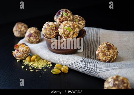 Energiekugeln aus trockenen Früchten, Pistazien, Hafer und Samen als Snack in einer Holzschale auf schwarzem Hintergrund Stockfoto