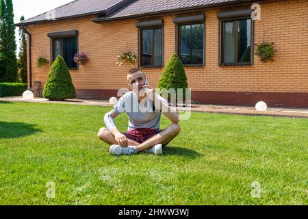 Mann mit amputiertem Arm und Prothese, der am Telefon auf dem Rasen sitzt Stockfoto