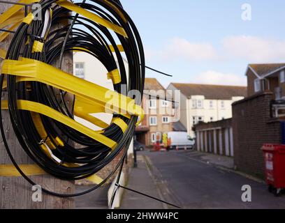 Telefonkabel aufgerollt und zusammen mit gelbem Klebeband im Freien auf der Straße gehalten. Stockfoto