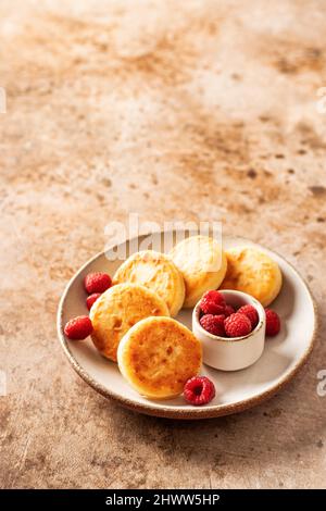 Hüttenkäse-Pfannkuchen, Syrniki mit frischer Himbeere auf texturiertem Hintergrund Stockfoto