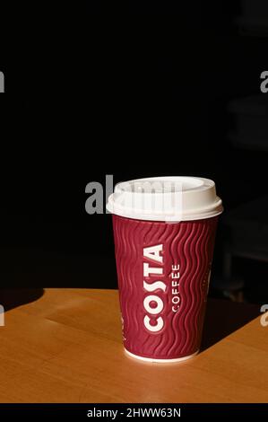 Carmarthen, Wales - März 2022: Papiertasse mit Kunststoffdeckel auf einem Tisch in einer Filiale von Costa Coffee. Keine Personen. Stockfoto