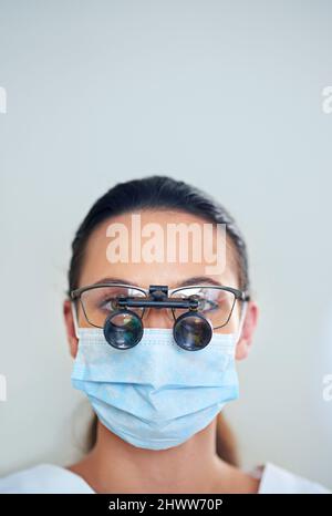 Sehen wir uns das einmal genauer an. Porträt einer jungen Zahnärztin mit Lupenbrille. Stockfoto