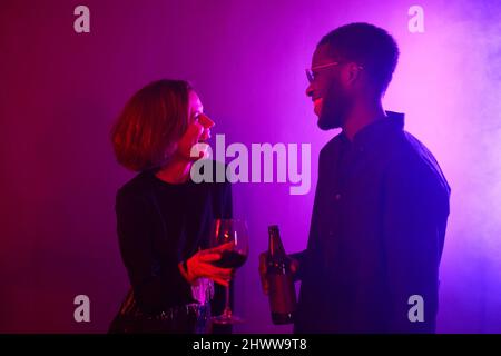 Minimal Taille up Porträt von jungen Paar lachen, während Party in Neonlicht genießen Stockfoto