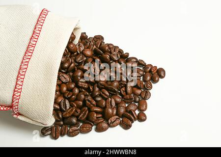 Kaffeebohnen verschüttet aus dem Beutel auf weißem Hintergrund. Isolieren. Geröstete Kaffeesamen. Stockfoto