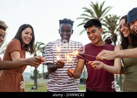 Multiethnische glückliche junge Freunde, die Spaß am Halten haben, funkeln am Festivalabend Stockfoto