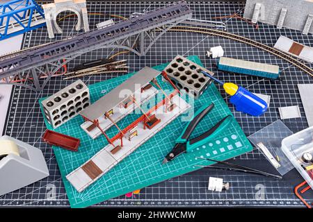 Bau einer Modelleisenbahnanlage. werkbank mit Modelleisenbahnstation Brückengleise und Landschaftswerkzeuge. Hobby Freizeitmodellierung c Stockfoto