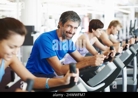 Ich bin fast fertig für den Tag. Eine kurze Aufnahme einer Reihe von Leuten, die im Fitnessstudio auf den Heimtrainern trainieren. Stockfoto