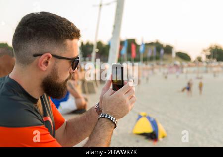 Mann fotografiert den Sonnenuntergang am Strand mit dem Smartphone Stockfoto