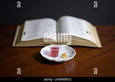 Christliches Abendmahl Sakramente, Wein und Brot mit offener Bibel im Hintergrund. Stockfoto