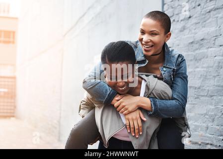 Du tragend im Herzen und im Geist. Aufnahme einer jungen Frau, die eine andere auf dem Rücken trug, während sie in der Stadt lachte. Stockfoto