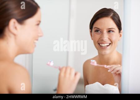 Zahngesundheit ist wichtig. Eine junge Frau, die vor dem Spiegel steht und sich die Zähne putzt. Stockfoto