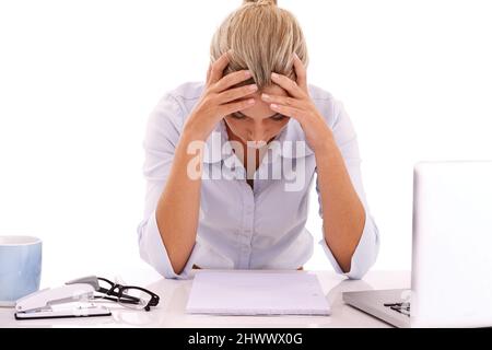 Die gestressten des Unternehmenslebens. Eine junge Geschäftsfrau, die mit dem Kopf in den Händen an ihrem Schreibtisch sitzt. Stockfoto