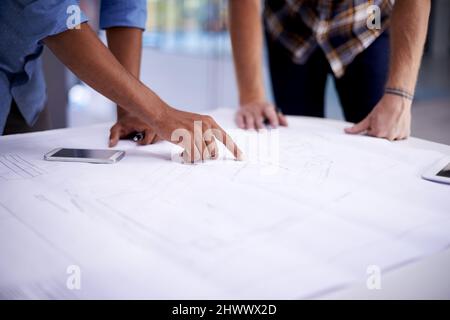 Gemeinsam großartige Dinge schaffen. Nahaufnahme von zwei jungen Architekten, die in einem Büro an Blaupausen arbeiten. Stockfoto