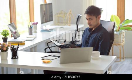 Fokussierter junger asiatischer Geschäftsmann arbeitet am Büroarbeitsplatz. Männlicher Chef sitzt in seinem privaten Zimmer. Stockfoto
