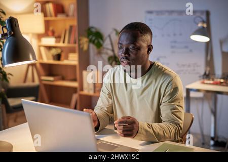 Afrikanischer junger Geschäftsmann, der an seinem Arbeitsplatz sitzt und online mit Kollegen auf dem Laptop spricht, und Geschäftstreffen im Büro hat Stockfoto