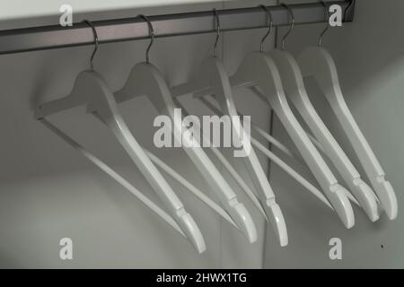 Nahaufnahme von weißen Kleiderbügeln. Kleidung auf einer Schiene im Kleiderschrank. Stockfoto