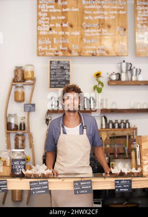 Immer ein freundliches Gesicht im Café. Porträt eines Baristas, der an einem Café-Tresen steht. Stockfoto