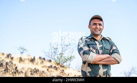 Selbstbewusster lächelnder indischer Soldat in Uniform, der mit gekreuzten Armen und Blick auf die Kamera steht - Konzept eines erfolgreichen, stolzen Soldaten und einer Besatzung. Stockfoto