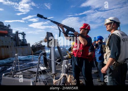 SÜDCHINESISCHES MEER (FEB 22, 2022) Gunners Mate 3. Klasse Keith Struzinski aus Lancaster, Pennsylvania, feuert während eines Wiederauffüllens auf See an Bord des Lenkrakenzerstörers USS Ralph Johnson (DDG 114) eine Schusslinie auf das Trockenfrachtschiff USNS Carl Brashear (T-AKE-7) der Lewis- und Clark-Klasse. Ralph Johnson ist der Task Force 71/Destroyer Squadron (DESRON) 15 zugeordnet, dem größten vorwärtseingesetzten DESRON der Marine und der wichtigsten Surface Force der US 7.-Flotte. (USA Navy Foto von Mass Communication Specialist 2. Class Samantha Oblander) Stockfoto