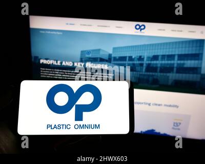 Person, die Mobiltelefon mit Logo der französischen Firma Compagnie Plastic Omnium SA auf dem Bildschirm vor der Business-Webseite hält. Konzentrieren Sie sich auf die Telefonanzeige. Stockfoto