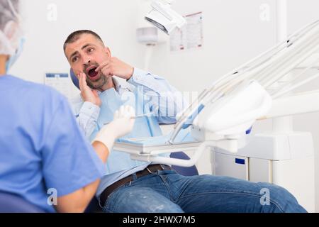 Unglücklicher amerikanischer Mann im medizinischen Stuhl beschwert sich über Zahnschmerzen Stockfoto