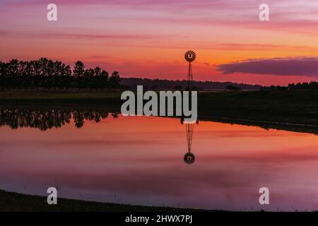 Alte Farm Windmühle in einem ländlichen Feld mit lebendigen Sonnenaufgangshimmel Stockfoto