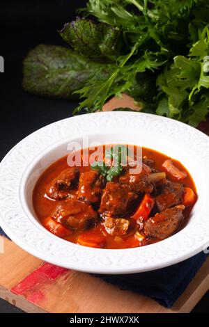 Speisekonzept hausgemachtes französisches Eintopf Rind Marengo in weißer Keramik-Suppenteller auf Holzbrett auf schwarzem Schieferstein-Hintergrund mit Kopierfläche Stockfoto