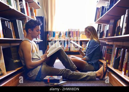 Gemeinsam studieren, aber getrennt. Zwei Studenten lesen in der Bibliothek separate Lehrbücher. Stockfoto