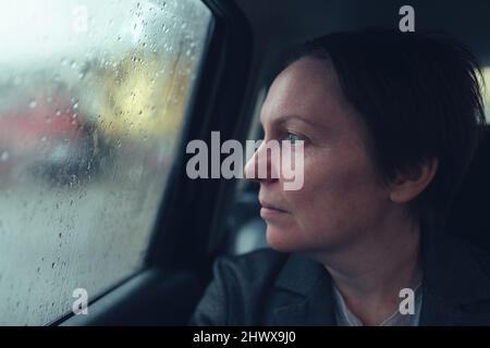 Geschäftsfrau im Taxi-Auto, die an einem regnerischen Tag aus dem Fenster schaut, selektiver Fokus Stockfoto